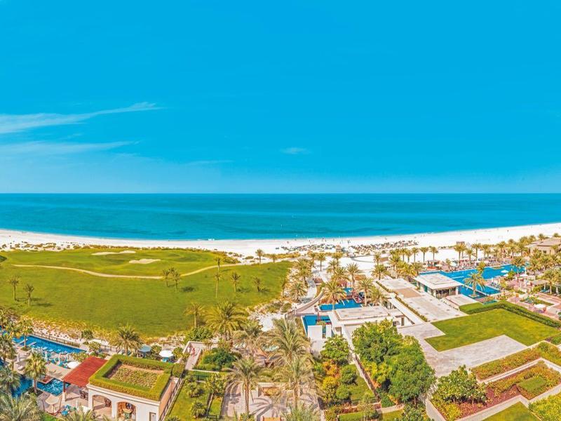 Blick auf ein Strandresort mit Pools, Gärten und mehrstöckigen Gebäuden unter blauem Himmel.