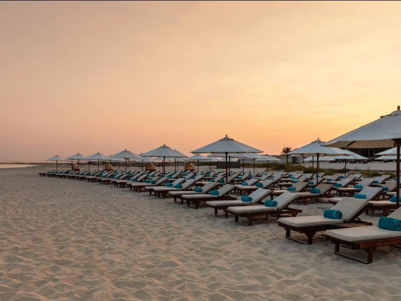 Strand mit Reihen von Liegestühlen und Sonnenschirmen bei Sonnenuntergang.