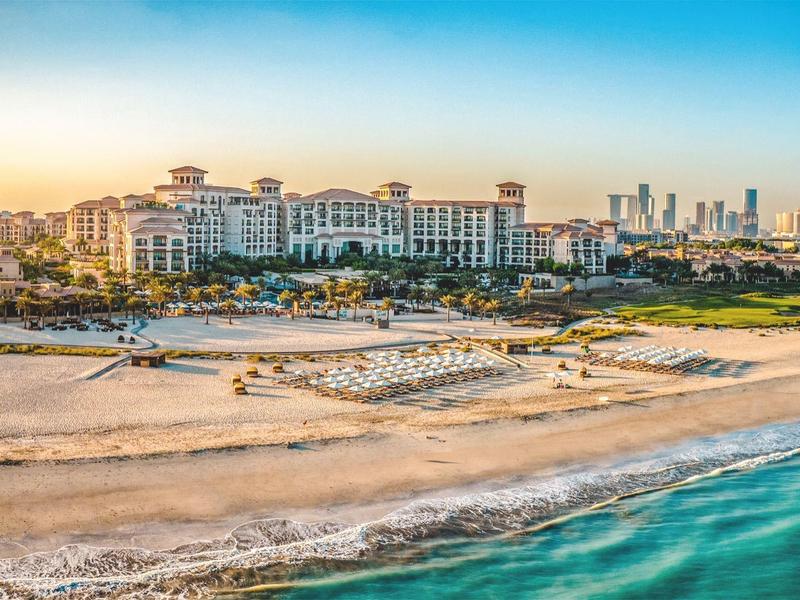 Weitläufiges Strandhotel mit Sandstrand und Sonnenschirmen bei Sonnenaufgang.