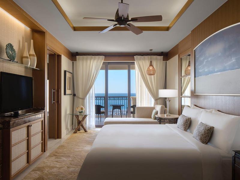 Modern eingerichtetes Hotelzimmer mit Doppelbett und Blick auf das Meer durch die Glasfenster.