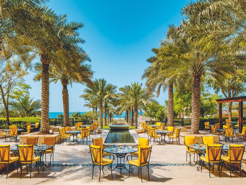 Freiluftrestaurant mit gelben Stühlen und Palmen an einem sonnigen Tag am Meer.