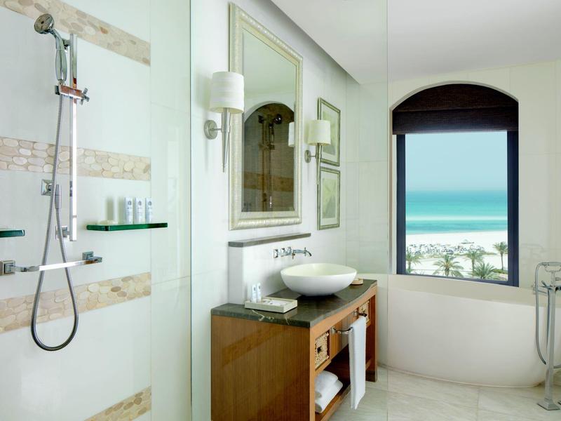 Hell gestaltetes Badezimmer mit Dusche, Waschbecken und Fenster mit Meerblick.