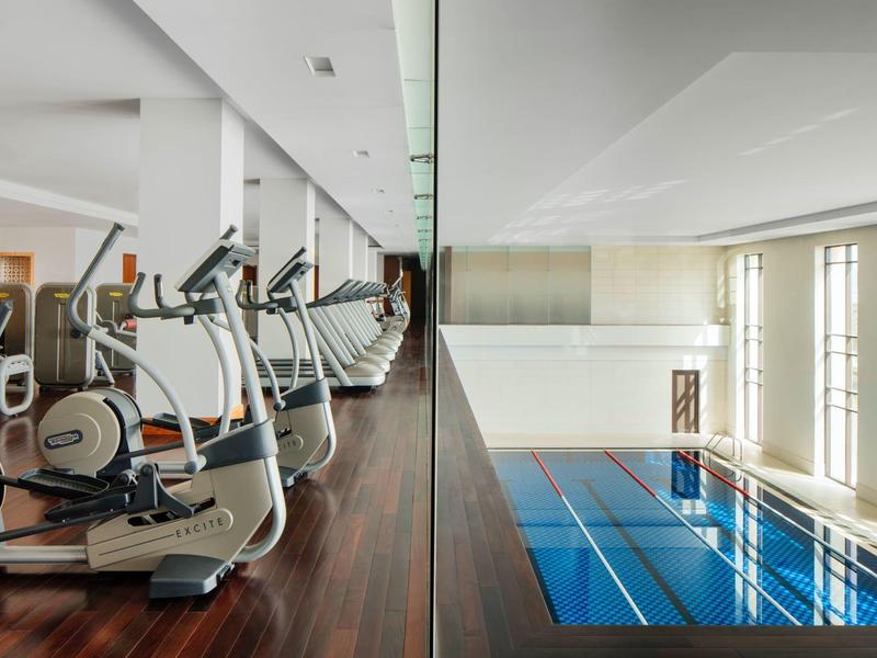 Moderner Fitnessraum und Schwimmbad mit Glaswand in hellem Innenraum.