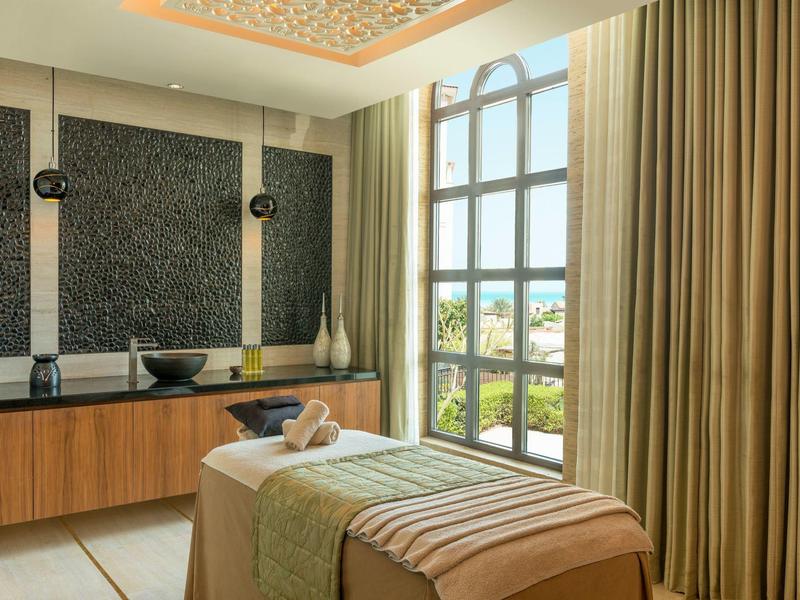 Helles Spa-Zimmer mit Behandlungsliege vor großem Fenster und Blick auf grüne Landschaft.