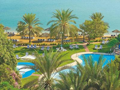 Hotelgarten mit Swimmingpools, Palmen und Blick aufs blaue Meer am Strand.