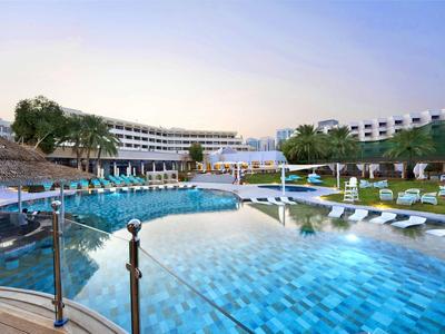 Moderner Hotelpool mit Liegestühlen und geschwungener Architektur bei klarem Himmel.