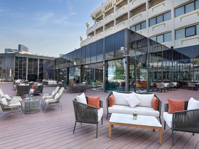 Moderner Hotel-Außenbereich mit komfortablen Sitzbereichen und Glaspavillon bei Tageslicht.