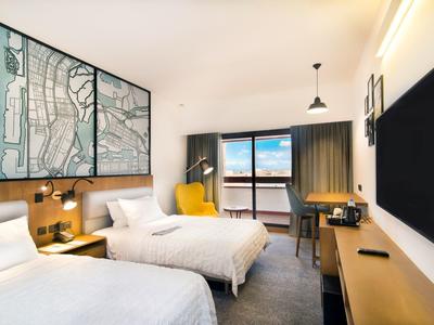 Modernes Hotelzimmer mit zwei Betten, großem Fenster, Schreibtisch und dekorativer Stadtkarte an der Wand.