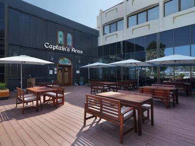 Außenbereich einer Terrasse mit Holztischen und Sonnenschirmen vor einem modernen Hotelgebäude.