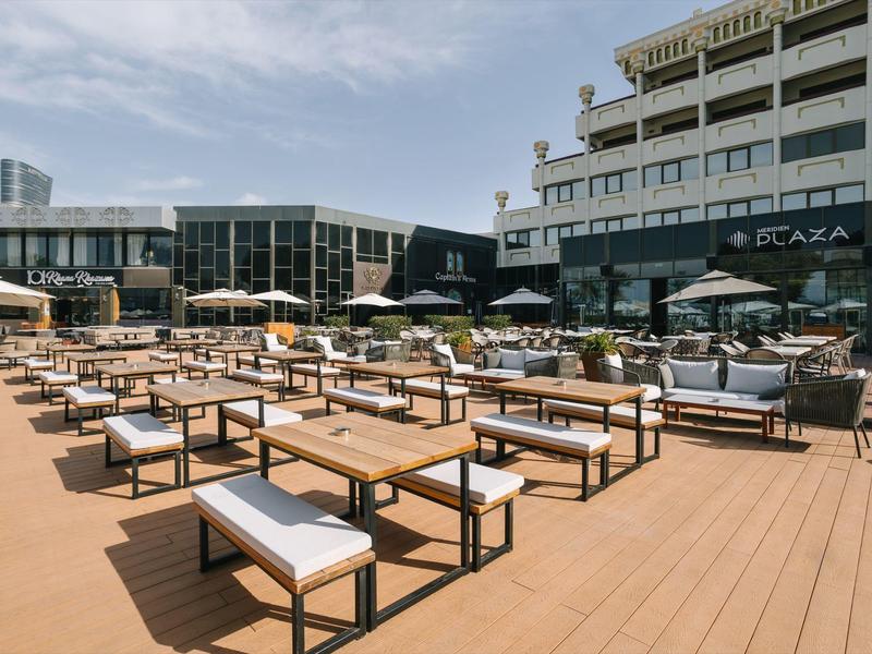 Moderne Terrasse mit vielen weißen Sitzmöbeln und Sonnenschirmen vor einem Hotelgebäude.