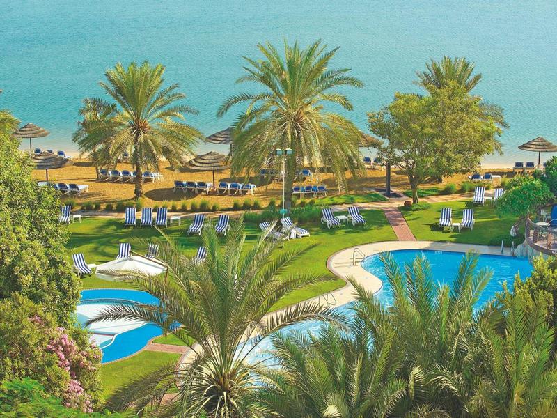 Hotelanlage mit Pools, Palmen und Liegestühlen am Meerufer.