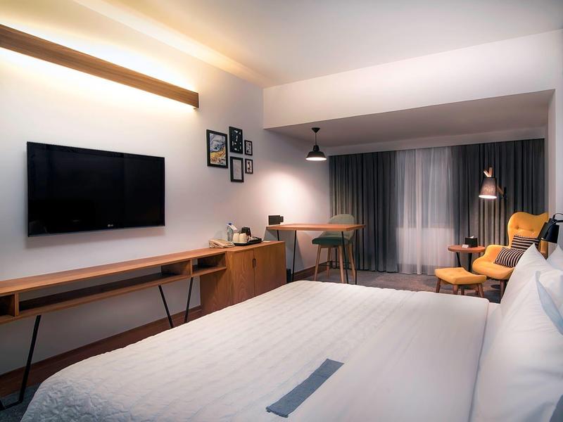 Modernes Hotelzimmer mit großem Bett, Flachbildfernseher und Arbeitsbereich mit Stuhl.