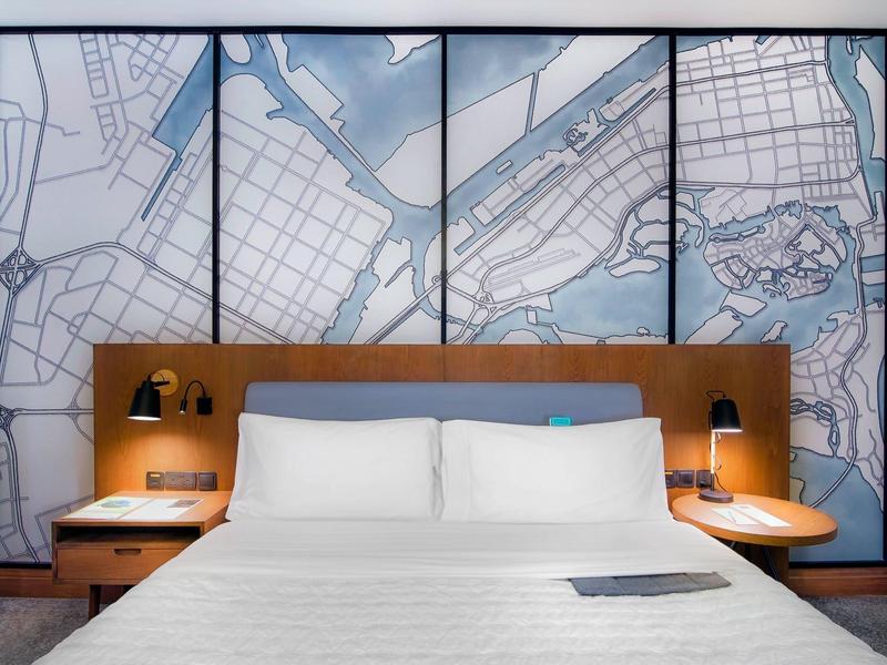 Modernes Hotelzimmer mit großem Bett, weißer Bettwäsche und einer Stadtkarte als Wanddekoration.