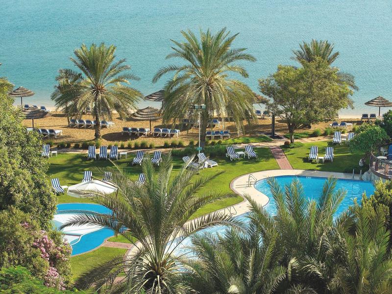 Blick auf einen Resort-Poolbereich mit Palmen und Blick auf das Meer im Hintergrund.