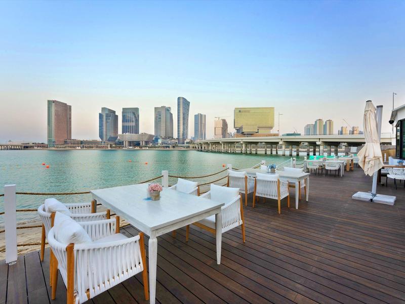 Terrasse mit weißen Möbeln und Blick auf einen Fluss und moderne Hochhäuser bei klarem Himmel