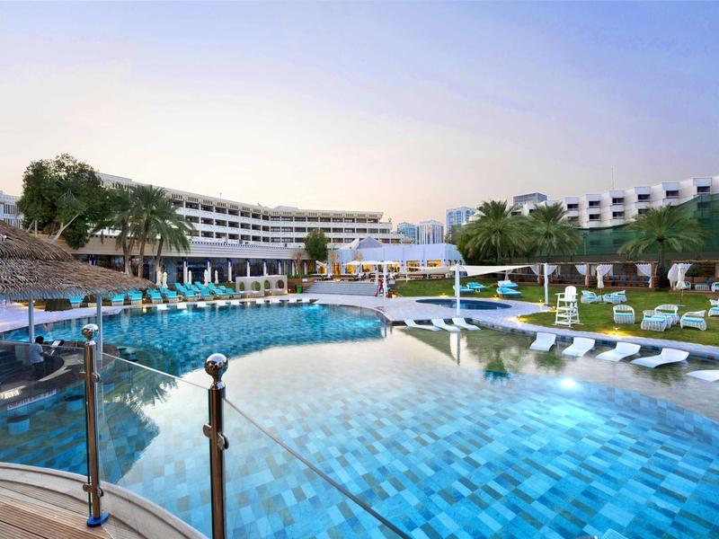 Moderner Hotelpool mit Liegestühlen und Sonnenschirmen in einer großzügigen Anlage bei Sonnenuntergang.