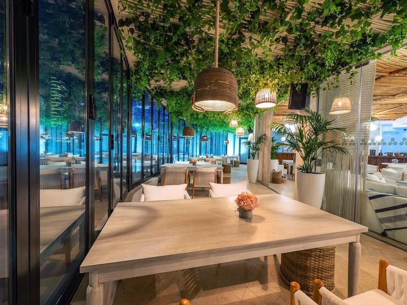 Moderner Außenbereich eines Restaurants mit Holztischen, Pflanzen und blauer Beleuchtung.