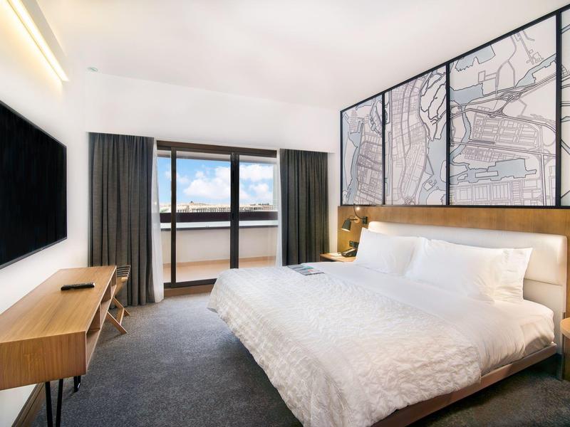 Modernes Hotelzimmer mit großem Bett, Schreibtisch und Balkon mit Meerblick.