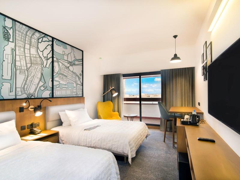 Modernes Hotelzimmer mit zwei Betten, großem Fenster und Stadtplan an der Wand.