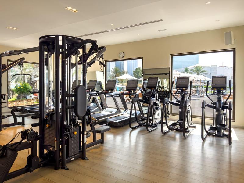 Heller Fitnessraum mit modernen Trainingsgeräten und großen Fenstern mit Stadtblick.