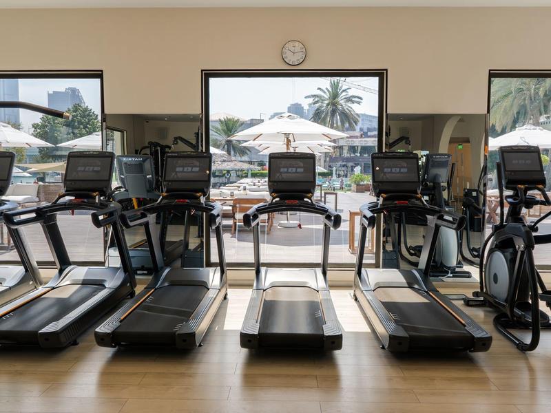 Moderne Fitnessgeräte in einem Trainingsraum mit Blick auf eine sonnige Terrasse und Pool