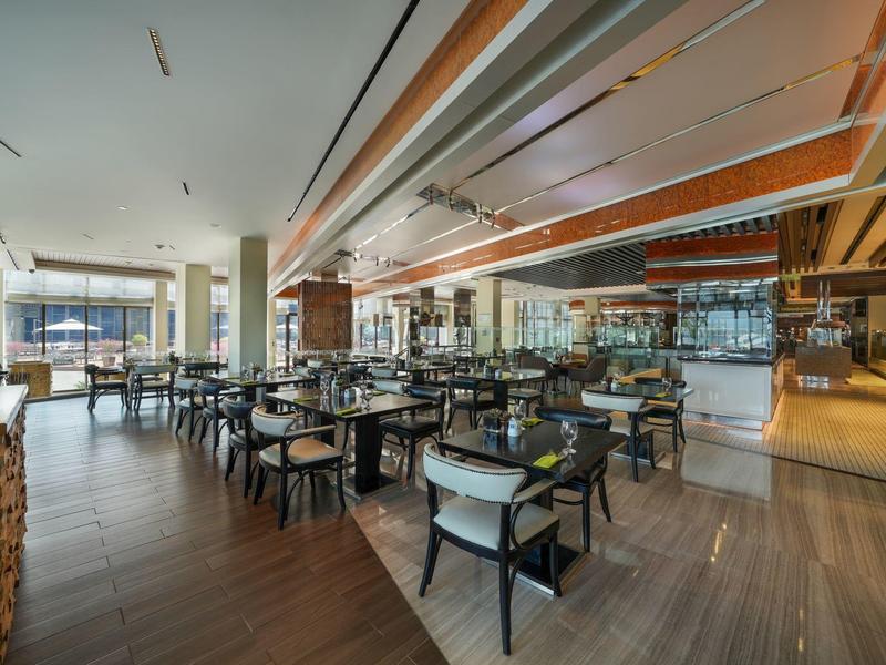 Modernes, helles Restaurant mit Holzboden, schwarzen Stühlen und großen Fenstern mit Blick auf die Terrasse.