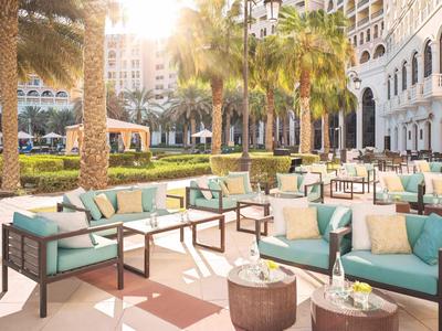 Sonnige Hotelterrasse mit bequemen Sitzmöbeln und Palmen im Hintergrund.