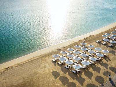 Sonnenliegen mit blauen Sonnenschirmen an einem ruhigen Strand bei Sonnenlicht.