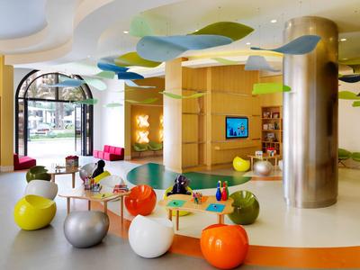 Bunte, moderne Hotellobby mit Sitzkugeln, großem Fenster und verspielter Deckenbeleuchtung.