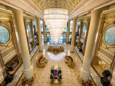 Großer Hotel-Luxussaal mit Marmorböden, Säulen und beeindruckendem Kronleuchter über Sofabereichen.