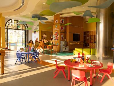 Heller, farbenfroher Kindergartenraum mit Kindertischen und Stühlen, Spielzeugen und großen Fenstern.