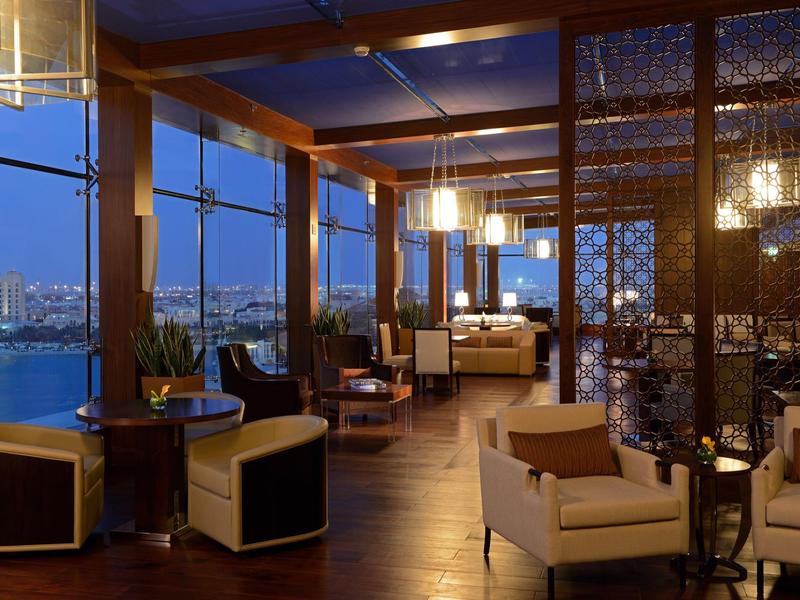 Lounge elegante con comodi posti a sedere e finestre panoramiche con vista sulla città e l'acqua di notte.