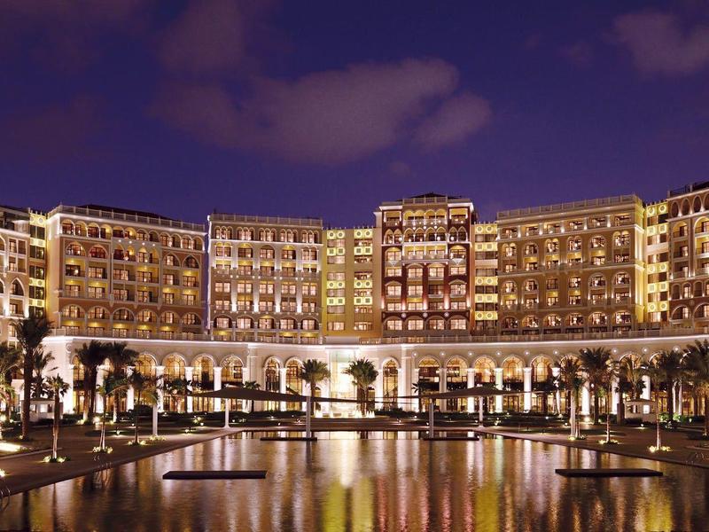 Grande hotel di lusso illuminato di notte con piscina e palme in primo piano