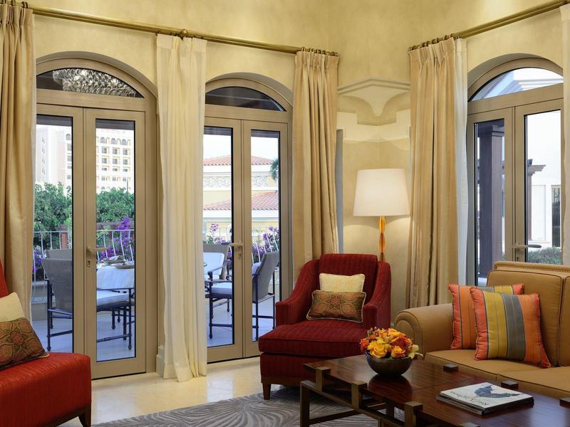 Camera d'hotel accogliente con poltrone rosse, tappeto chiaro e vista sulla terrazza attraverso grandi finestre.