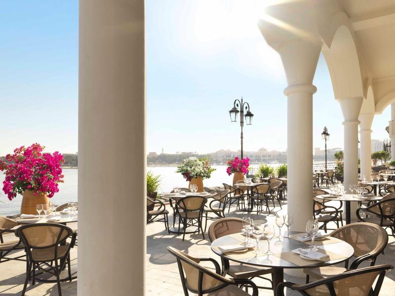Terrazza con tavoli e sedie sotto archi bianchi con vista su un fiume.