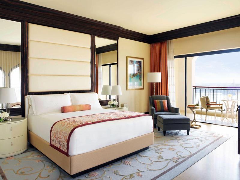 Camera d'hotel luminosa con letto grande, poltrona e balcone con vista sul mare.