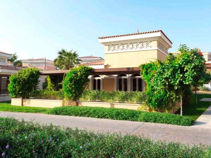 Edificio dell'hotel giallo in stile mediterraneo con palme e aree verdi curate