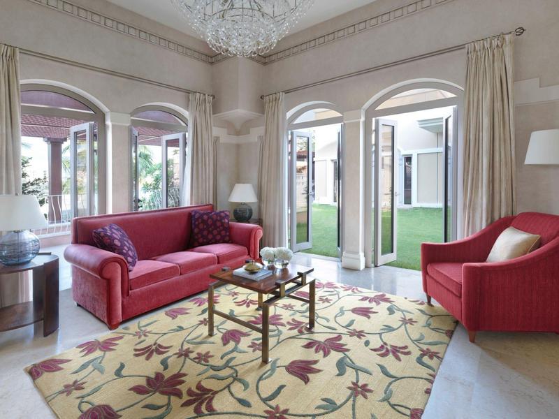 Soggiorno luminoso con divano rosso, poltrone e grande tappeto davanti a porte finestre.