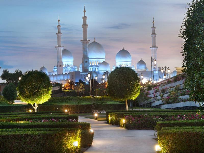 Sentiero del giardino illuminato con vista su una moschea al crepuscolo.