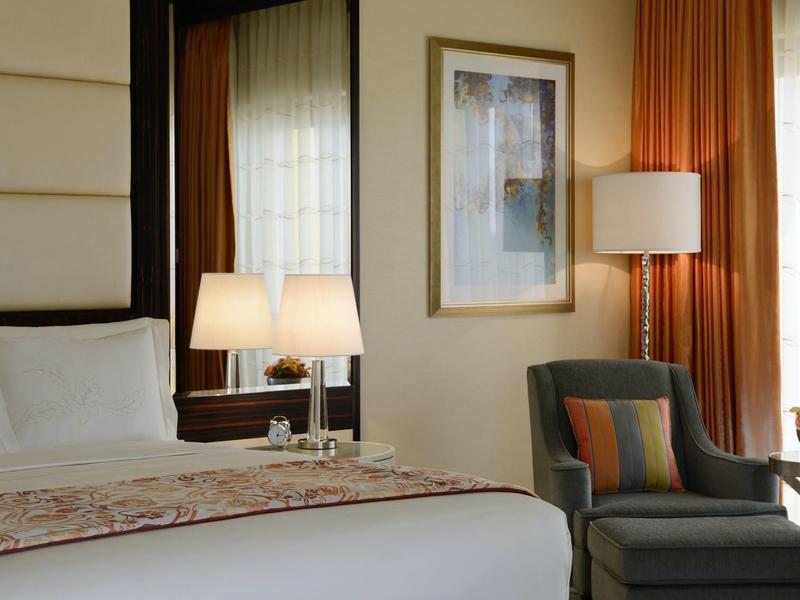 Camera d'hotel accogliente con letto grande, lampade da comodino e poltrona vicino alla finestra.