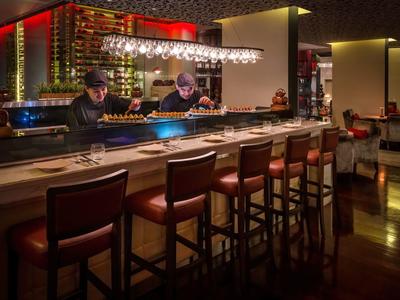 Modern hotel bar area with leather stools, bar counter, and bartenders at work.