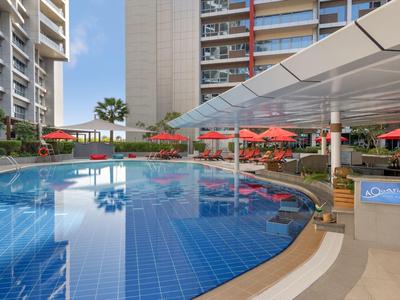 Modern hotel pool with blue tiles, red umbrellas, and high-rise buildings in the background.