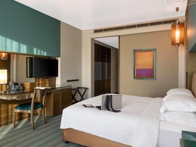 Modern hotel room with double bed, desk, TV, and minimalist decor.