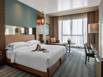 Modern hotel room with double bed, seating area, and large window with curtains.