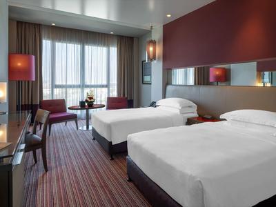 Modern hotel room with two single beds, chairs, and large window.