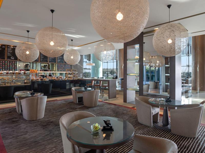 Modern hotel lounge area with round tables, armchairs, and large decorative hanging lights.