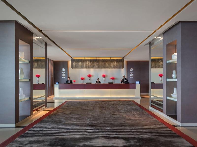 Modern, elegant hotel lobby reception with white counter and red flowers on the table.