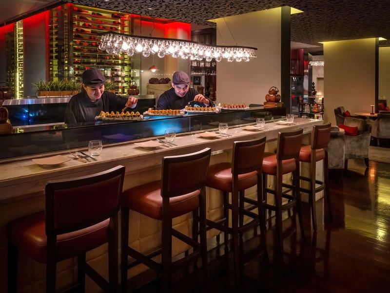 Modern hotel bar area with leather stools, bar counter, and bartenders at work.