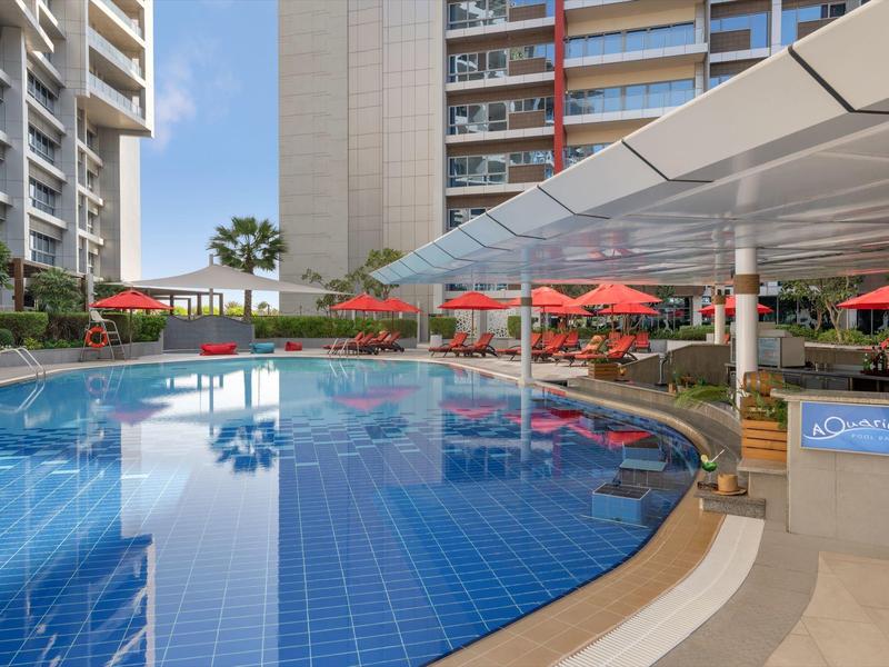 Modern hotel pool with blue tiles, red umbrellas, and high-rise buildings in the background.