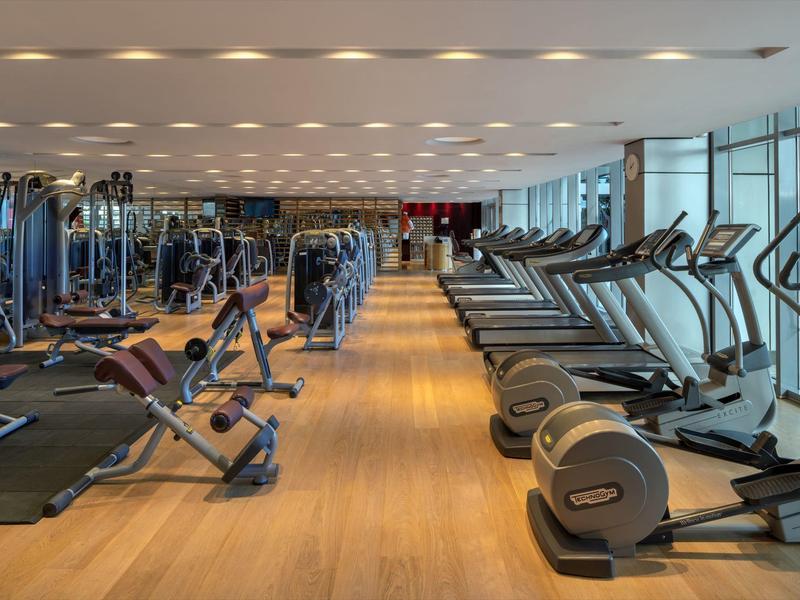 Large gym with modern equipment and wooden flooring in a hotel.